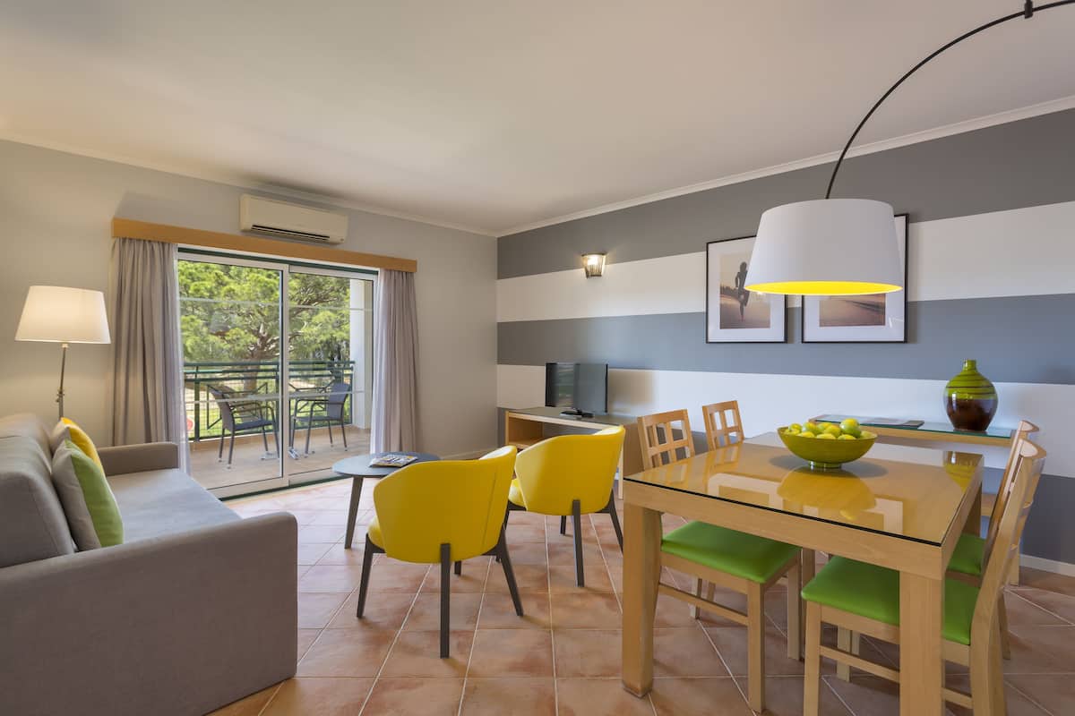 A modern living room with a sofa, yellow chairs, a glass dining table, and a TV.