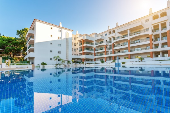 Un hotel moderno con una gran piscina, varios balcones y un cielo despejado.