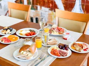 A breakfast buffet with various dishes, including eggs, fruits, and pastries, on a wooden table with a white tablecloth.