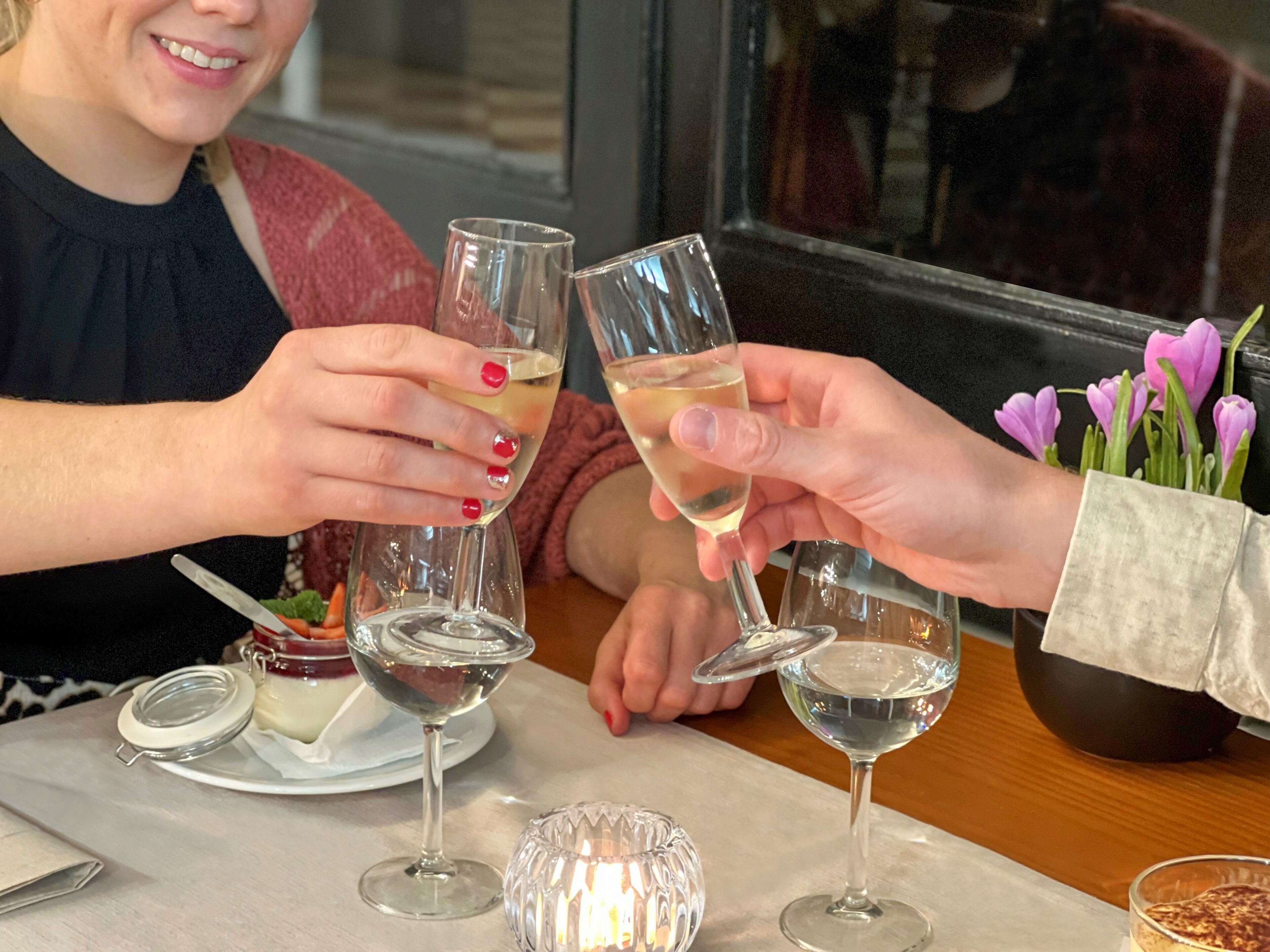 Een eettafel met twee wijnglazen, een kaars en een bloemenvaas.