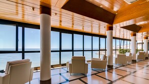 A spacious lobby with large windows offering a view of the sea, several seating areas, and a tiled floor. - Hotel Sol e Mar - Adults Only (Albufeira)