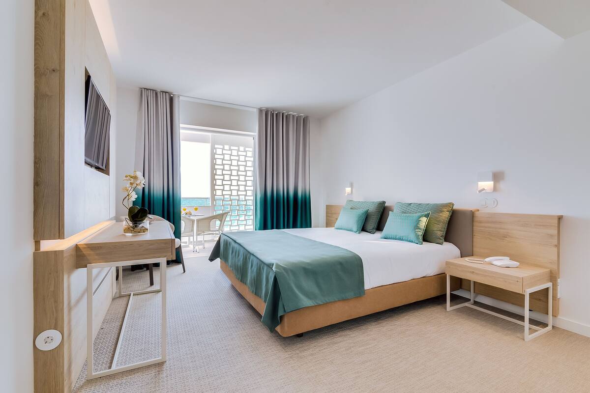 A modern hotel room with a bed, bedside table, desk, and chair.
