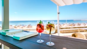 Two glasses of drinks on a wooden table with a view of the beach and ocean in the background.