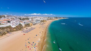 An aerial view of a coastal town with a wide sandy beach, a clear blue sea, and buildings along the coastline. - Hotel Sol e Mar - Adults Only (Albufeira)
