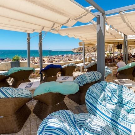A beachside lounge with wicker furniture and striped cushions, overlooking the sea.