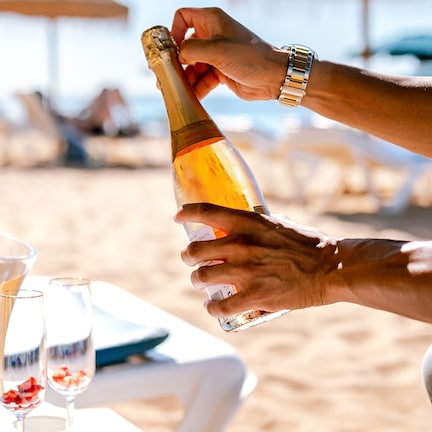 A person pouring champagne into a glass on a beach.