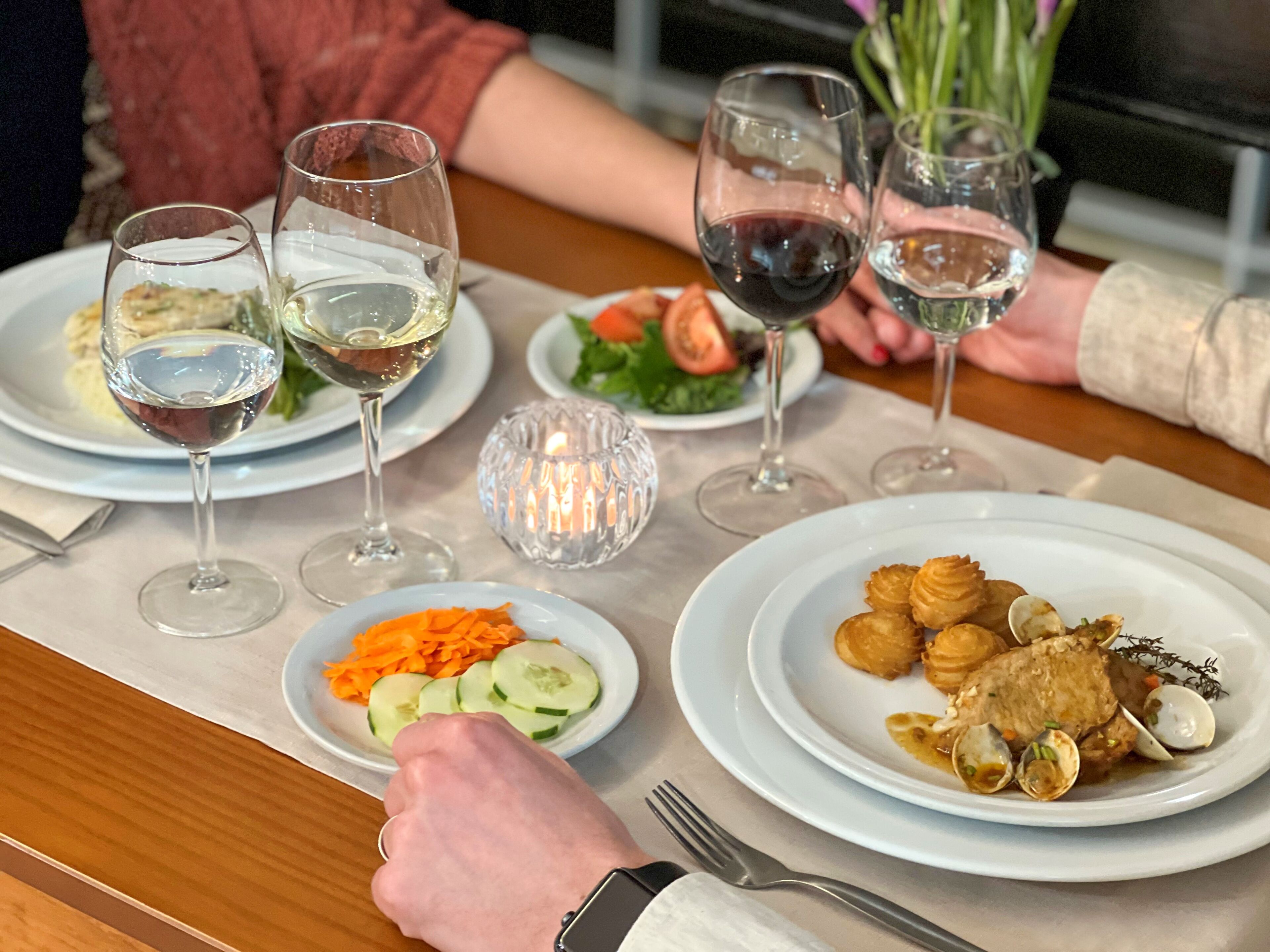 A dining table with plates of food, wine glasses, and a candle.