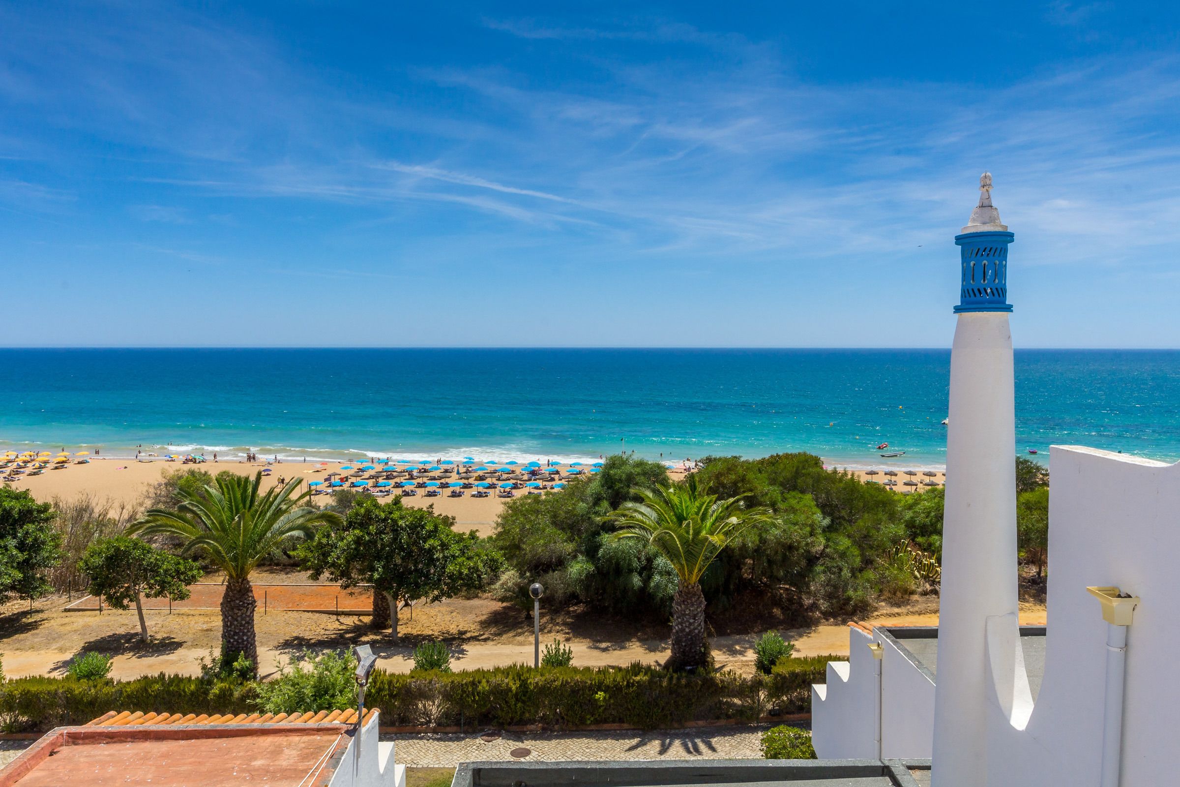 Blick auf einen Strand mit einem weißen Gebäude und einem blauen Turm, Palmen und einem klaren Himmel.