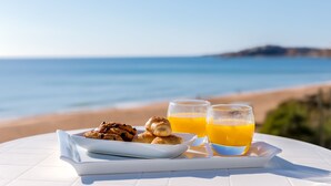 En frukostuppsättning med bakverk och apelsinjuice på ett vitt bord med utsikt över stranden.