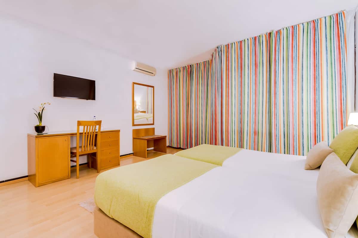 Hotellihuone, jossa on sänky, työpöytä, tuoli, peili ja televisio.
