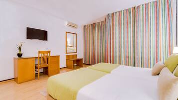 A hotel room with a bed, a desk, a chair, a mirror, and a TV.