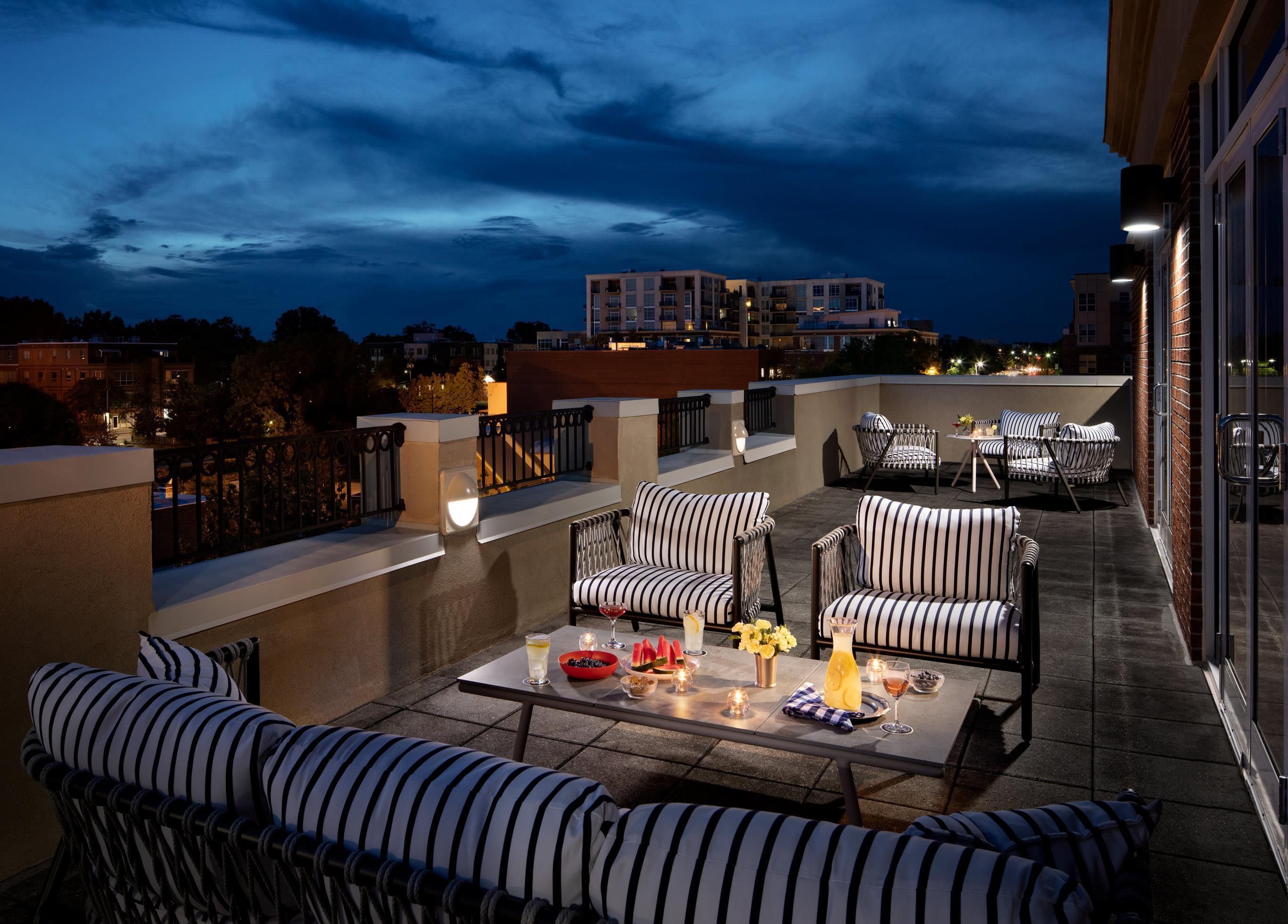 Une terrasse sur le toit avec des sièges extérieurs, une table avec des boissons et une vue sur la ville au crépuscule.