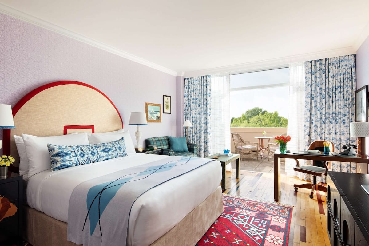 A hotel room with a large bed, a desk, a chair, and a view of the outdoors.