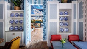 A room with blue patterned wallpaper, shelves with blue and white plates, a red chair, and a table with a vase.