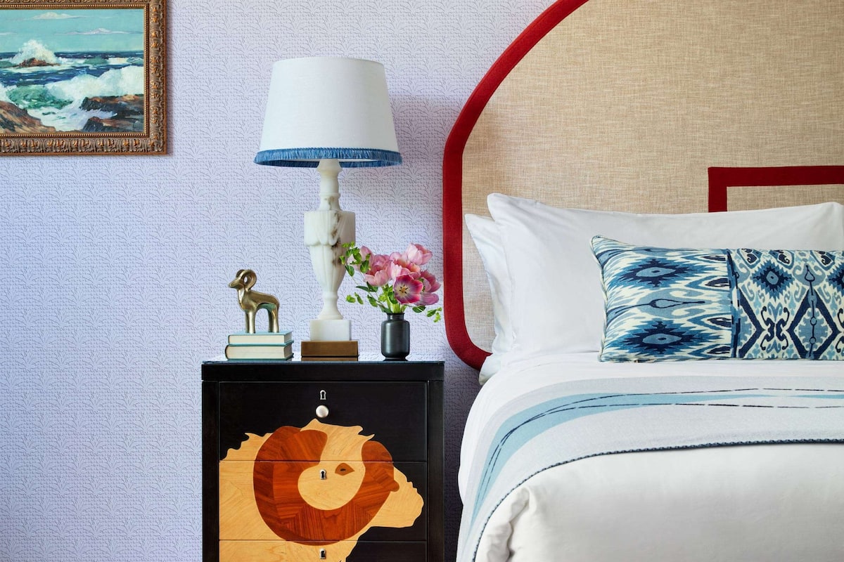 A bedroom with a bed, a nightstand with a lamp, a decorative cabinet, and a framed picture on the wall.