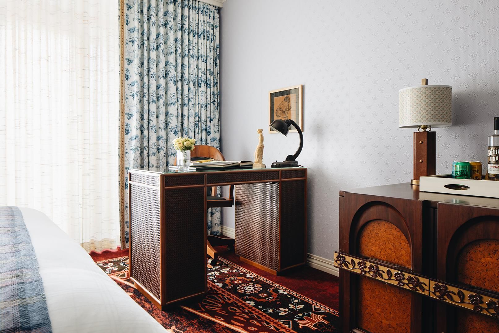 Una habitación de hotel con una cama, una mesita con una lámpara, un jarrón decorativo y un cuadro en la pared.