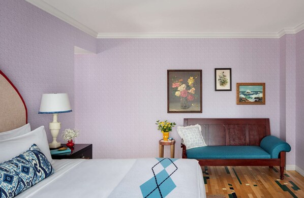 Un cuarto de hotel con una cama, un sofá, una mesita de noche con una lámpara y dos cuadros en la pared.