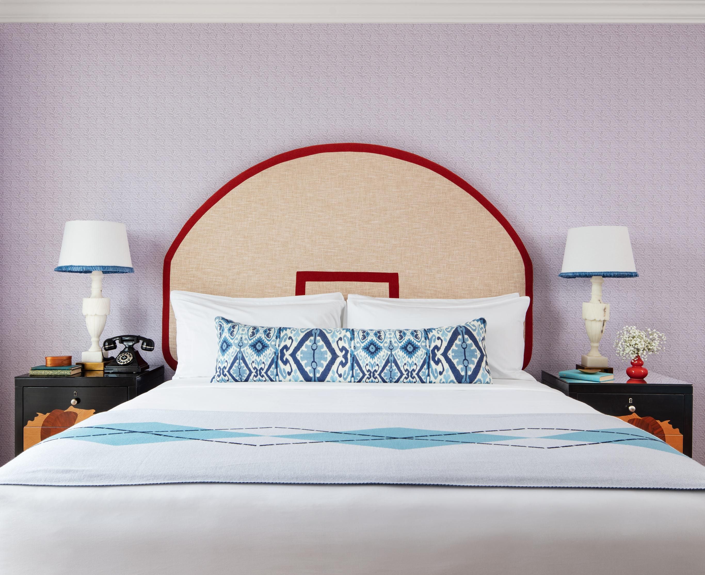 Una cama bien hecha con una colcha estampada, dos mesitas de noche con lámparas, un teléfono, libros y un florero con flores.