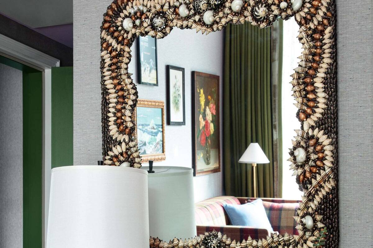 A mirror with a decorative frame, a lamp, a vase with flowers, and a bookshelf with books.
