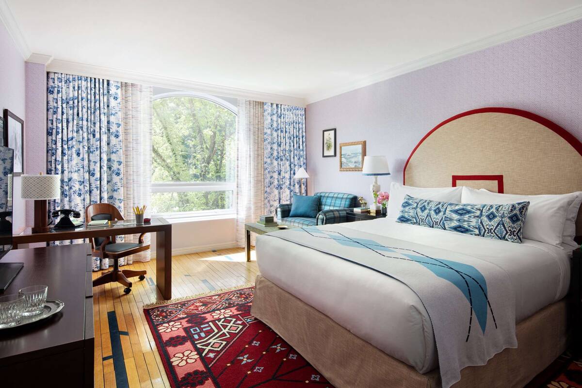 A hotel room with a bed, a desk, a chair, a lamp, and a window with curtains.