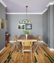 Un comedor con una mesa de madera, cuatro sillas, un florero con flores y cuadros en la pared.