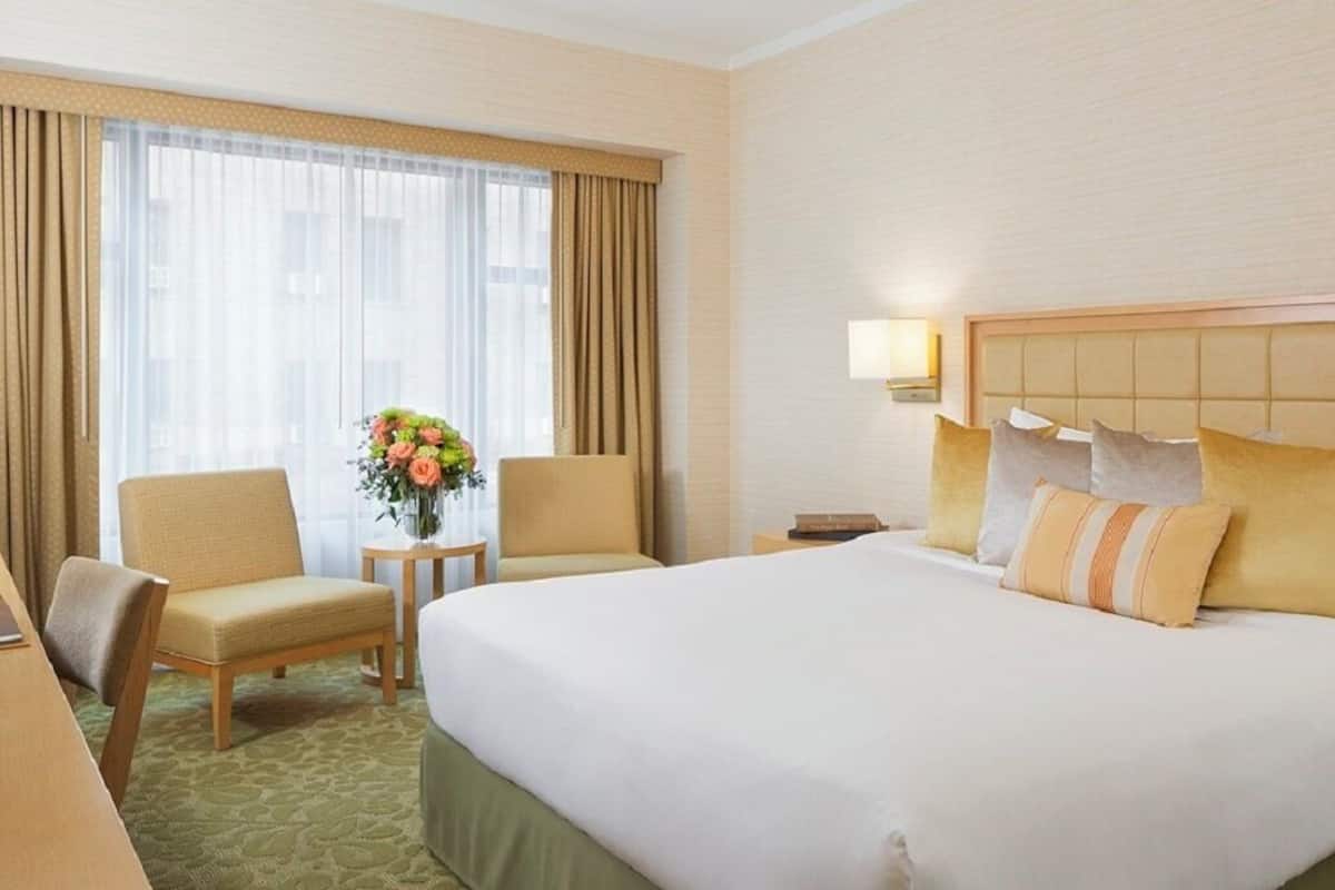 A hotel room with a large bed, two armchairs, a small table with a vase of flowers, and a nightstand with a lamp.