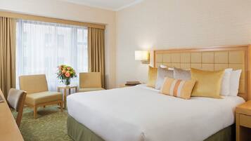A hotel room with a large bed, two armchairs, a small table with a vase of flowers, and a nightstand with a lamp.