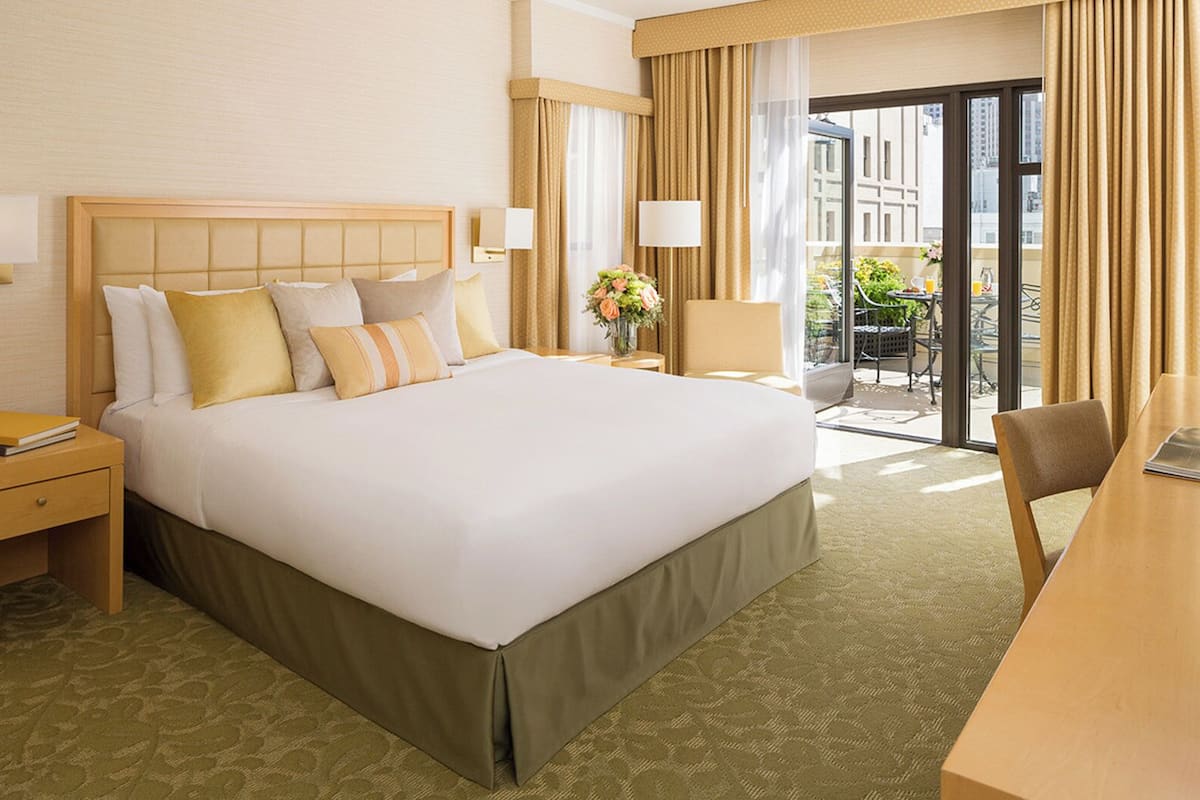 A hotel room with a large bed, a desk, a chair, a nightstand, and a view of the outdoors.