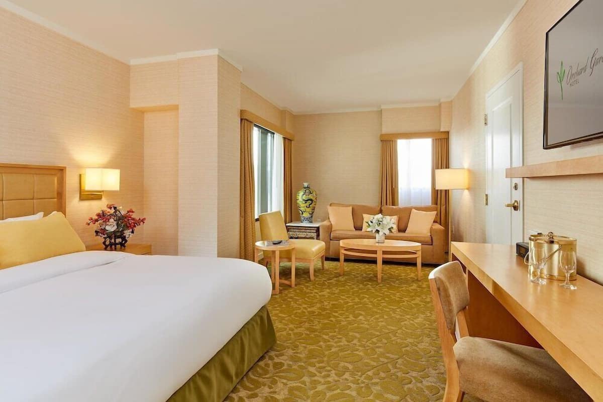 A hotel room with a large bed, a sofa, a small table, and a desk.