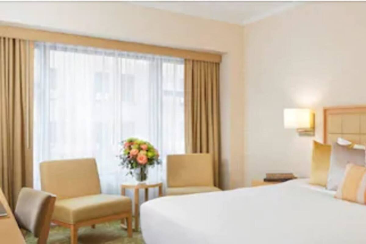A hotel room with a large bed, two chairs, a small table with a vase of flowers, and a nightstand with a lamp.