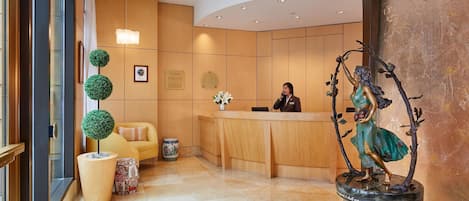 A reception area with a wooden reception desk, a receptionist, a statue, and a potted plant.