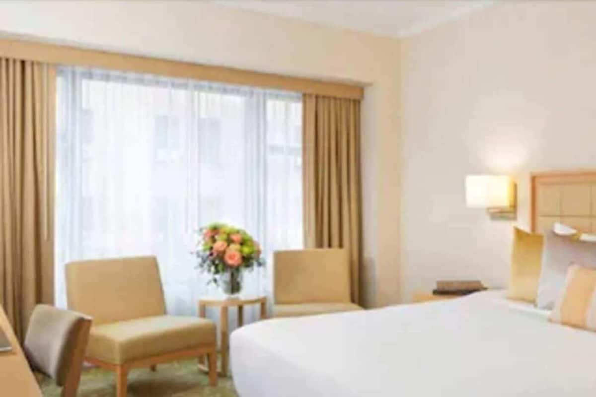 A hotel room with a large bed, two armchairs, a small table with a vase of flowers, and a nightstand with a lamp.