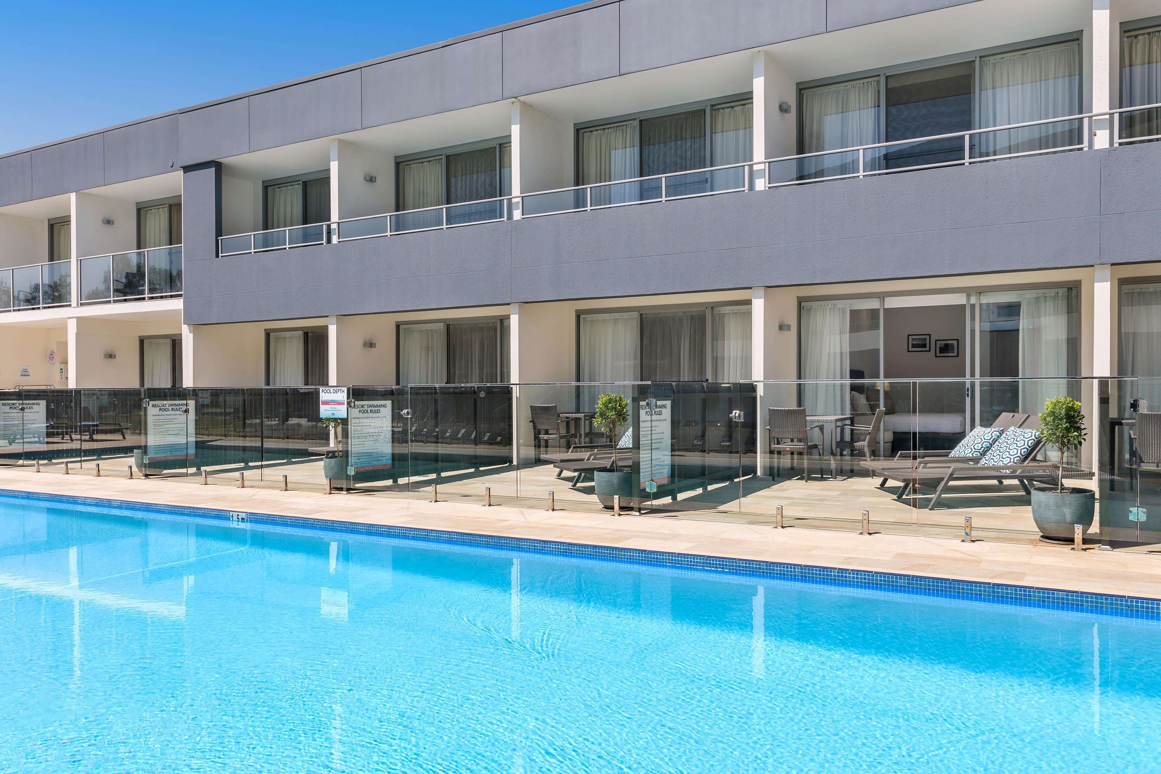 Un hotel moderno con piscina, diversi balconi e aree salotto all'aperto.