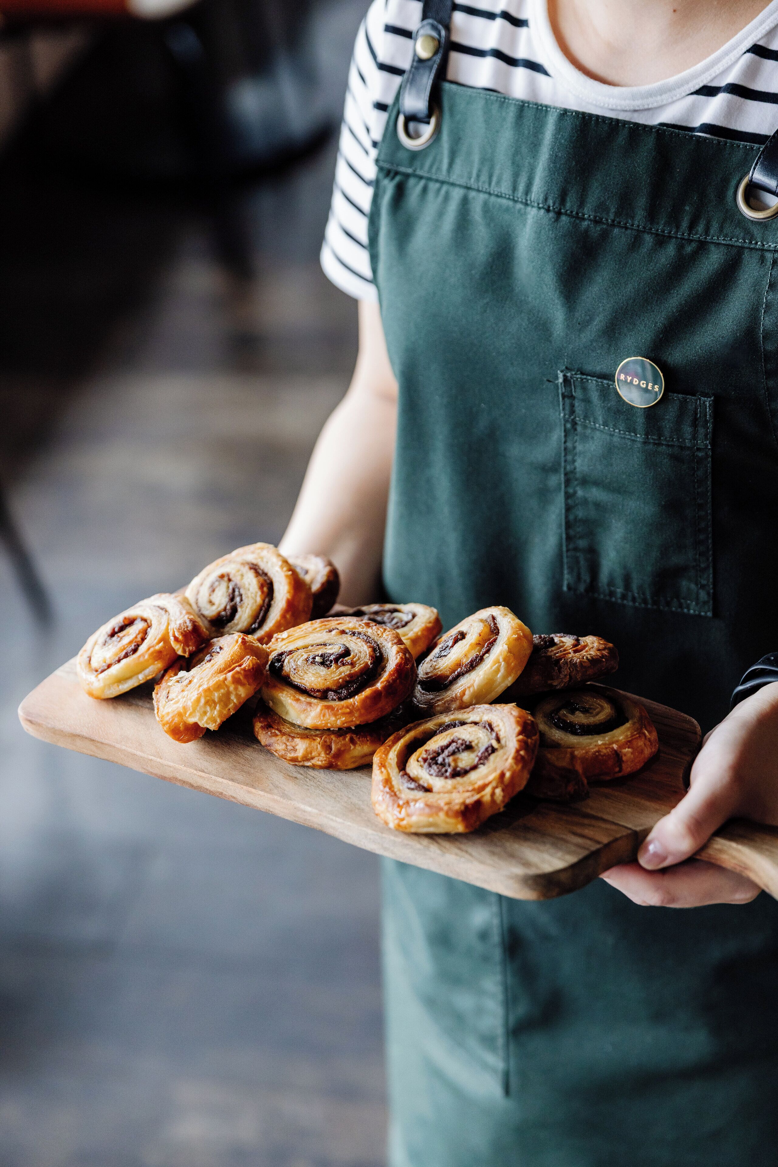 A person holding a wooden board with cinnamon rolls.