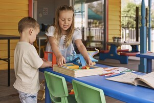 Dos niños sentados a una mesa con un rompecabezas de madera y materiales de colorear.