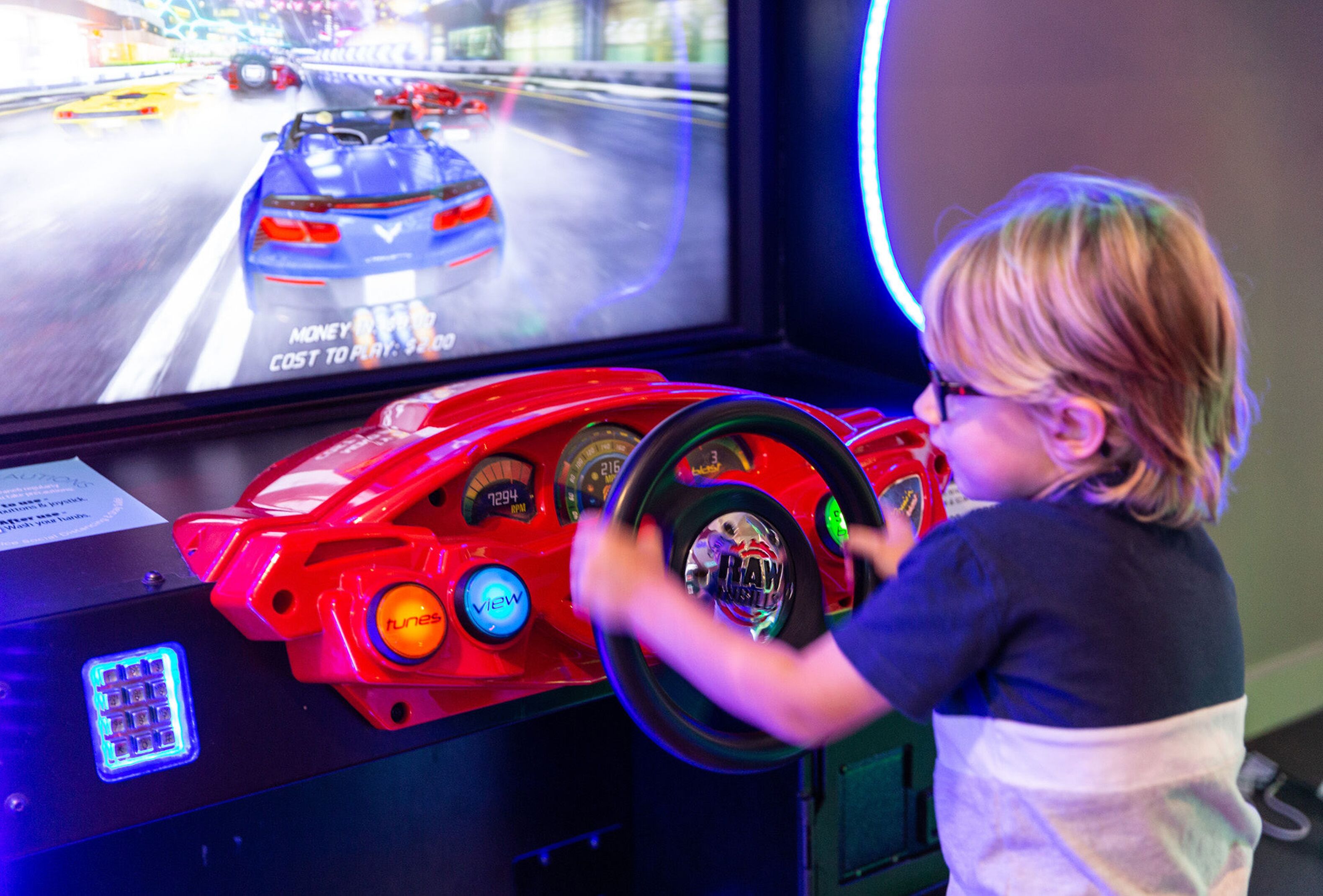 Ein Kind spielt ein Rennspiel auf einem Simulator mit einem Lenkrad und einem Bildschirm, der einen Rennwagen zeigt.