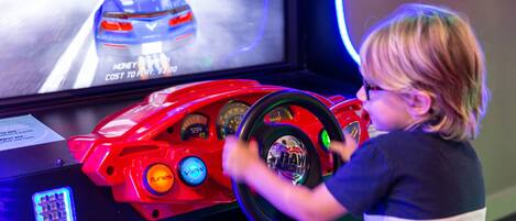 Ein Kind spielt ein Rennspiel auf einem Simulator mit einem Lenkrad und einem Bildschirm, der einen Rennwagen zeigt.