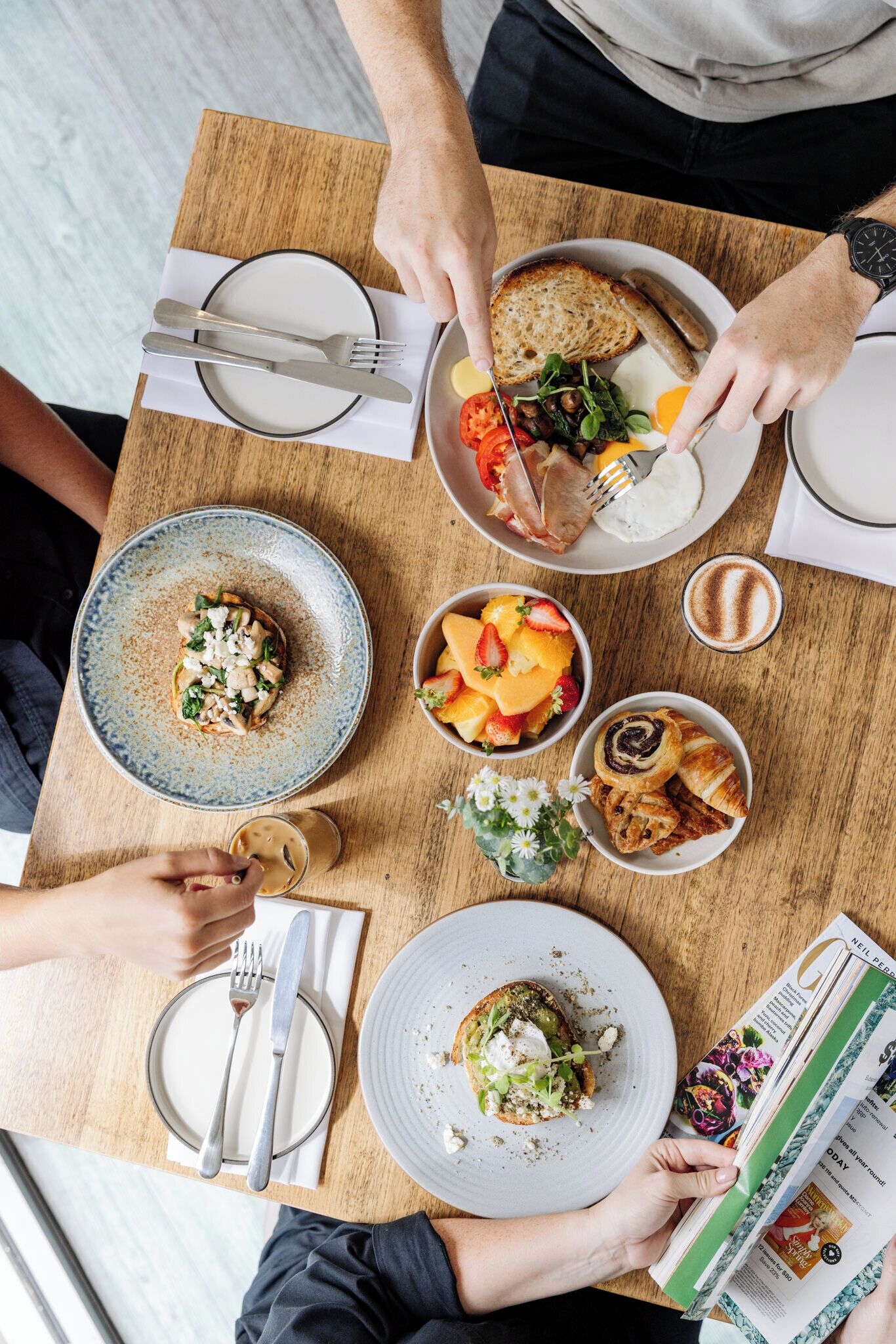 A dining table with plates of food, utensils, and a magazine.