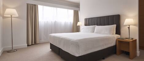 Habitación de hotel con una cama grande, dos lámparas de noche, una ventana con cortinas y suelo alfombrado.