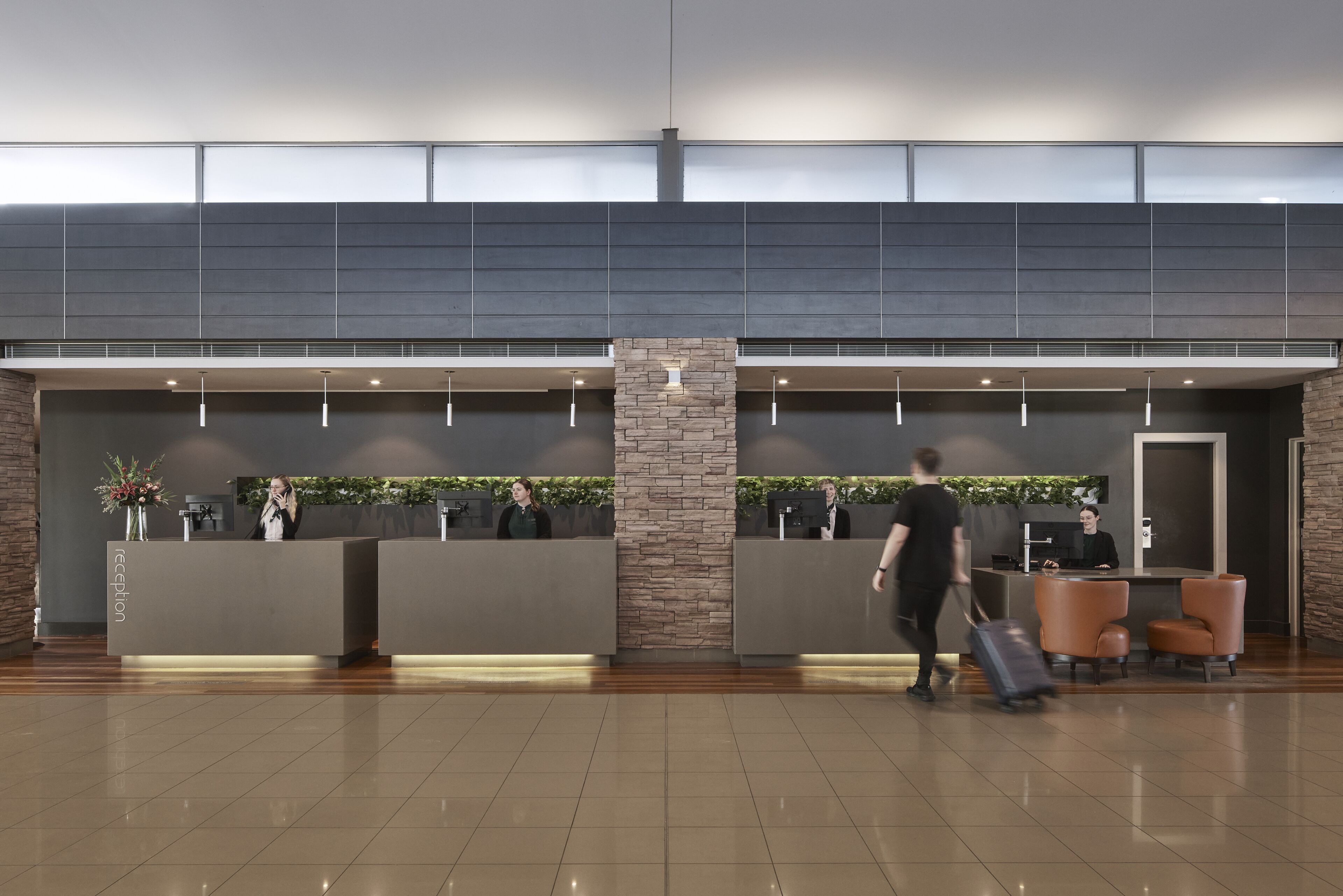 A modern reception area with a stone pillar, reception desks, and a seating area with leather chairs.