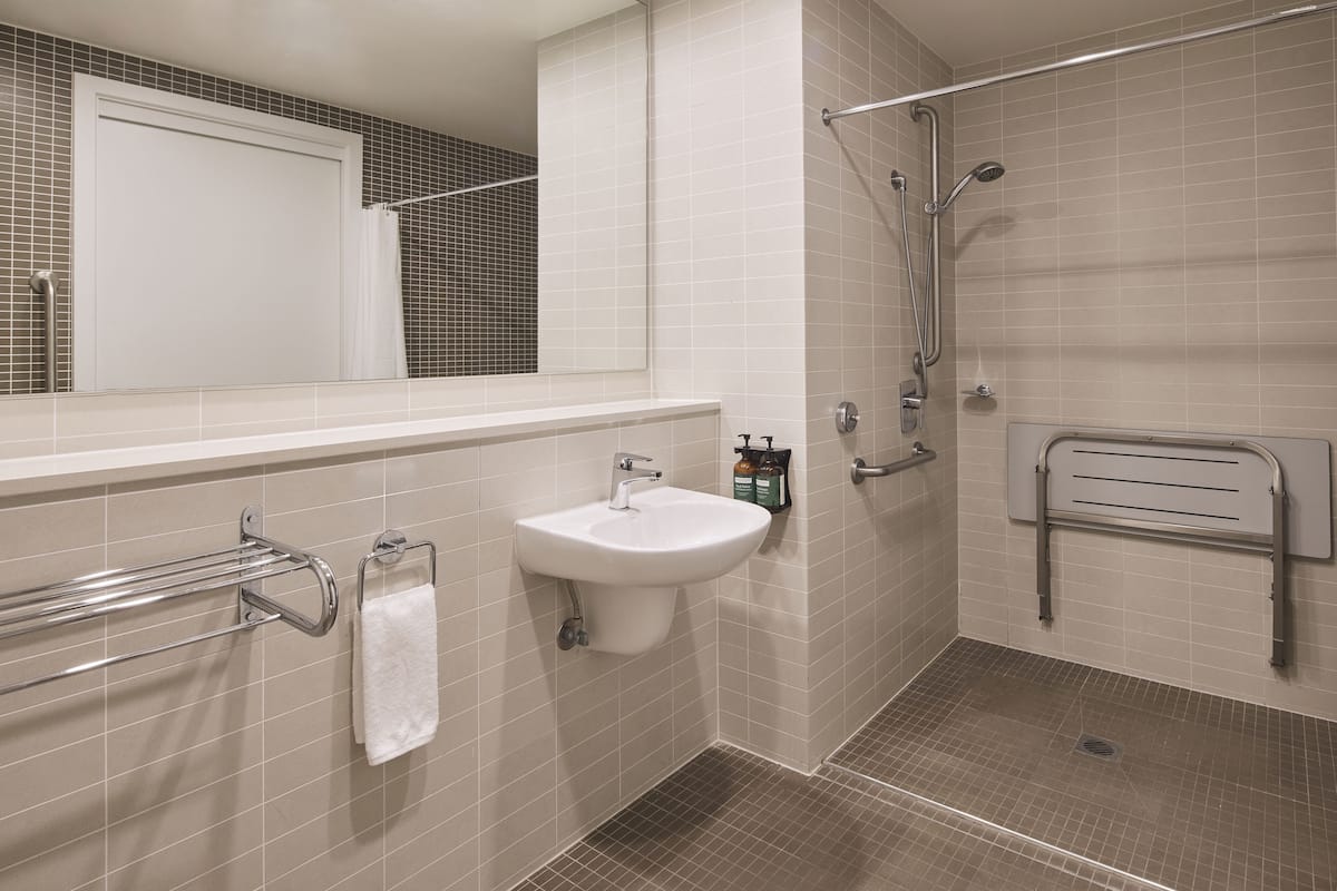 A modern bathroom with a white sink, a towel rack, a shower with a handheld showerhead, and a grab bar.