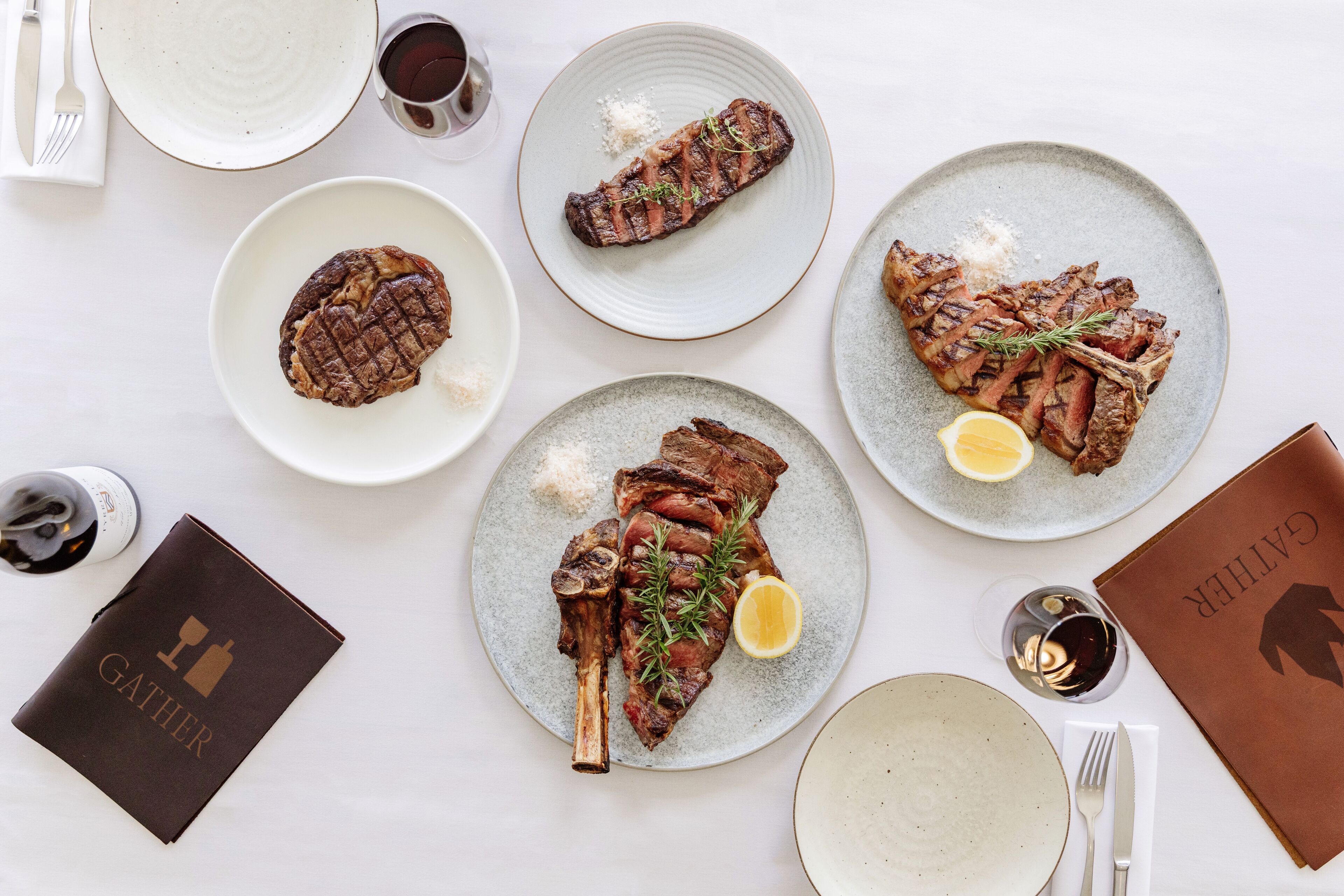 Mesa posta com bife, uma garrafa de vinho e um cardápio encadernado em couro.