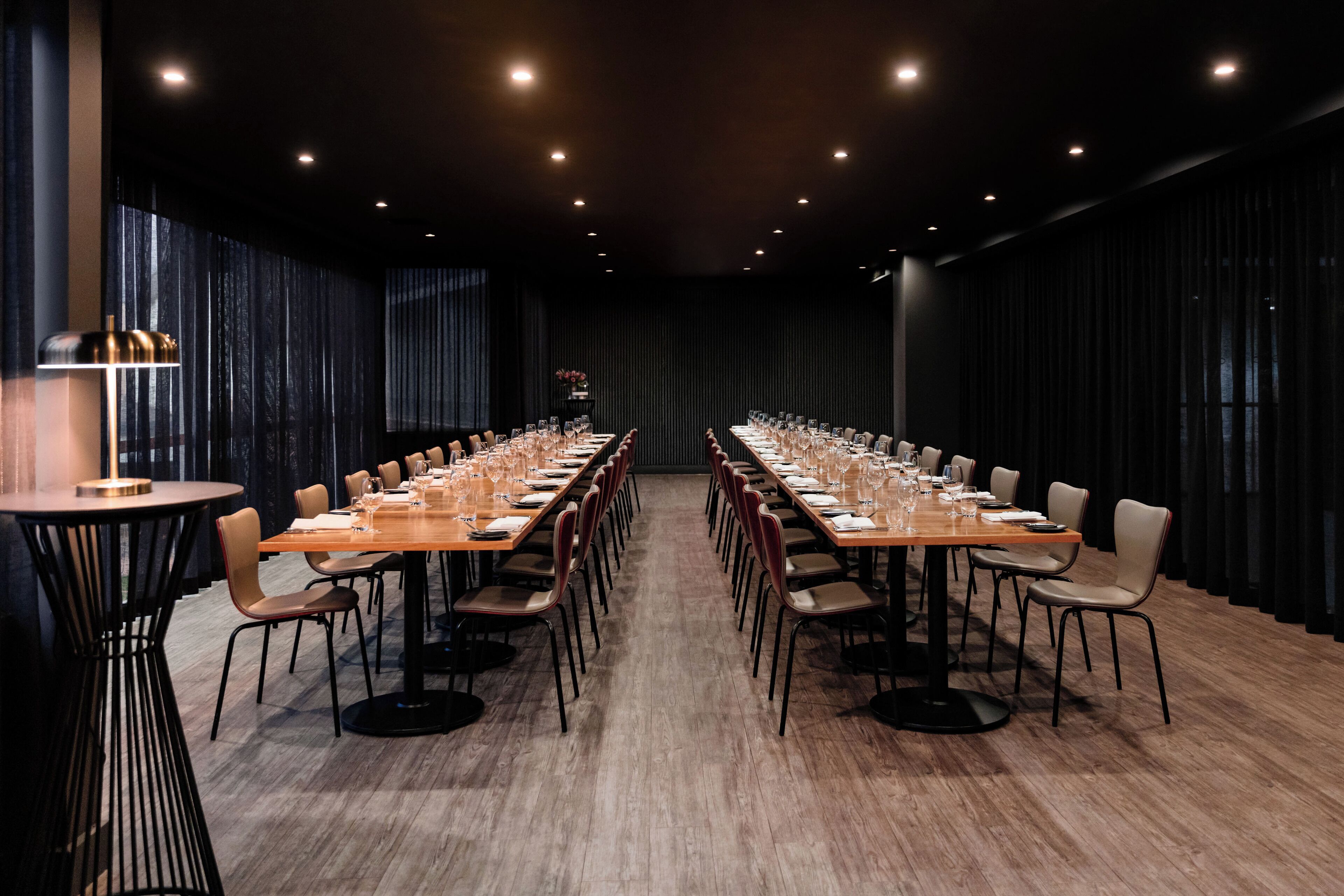 A conference room with a long table set for a meeting, surrounded by chairs, with a modern chandelier and a large window with curtains.