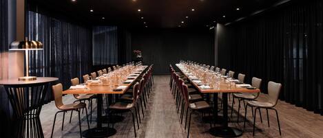 A conference room with a long table set for a meeting, surrounded by chairs, with a modern chandelier and a large window with curtains.