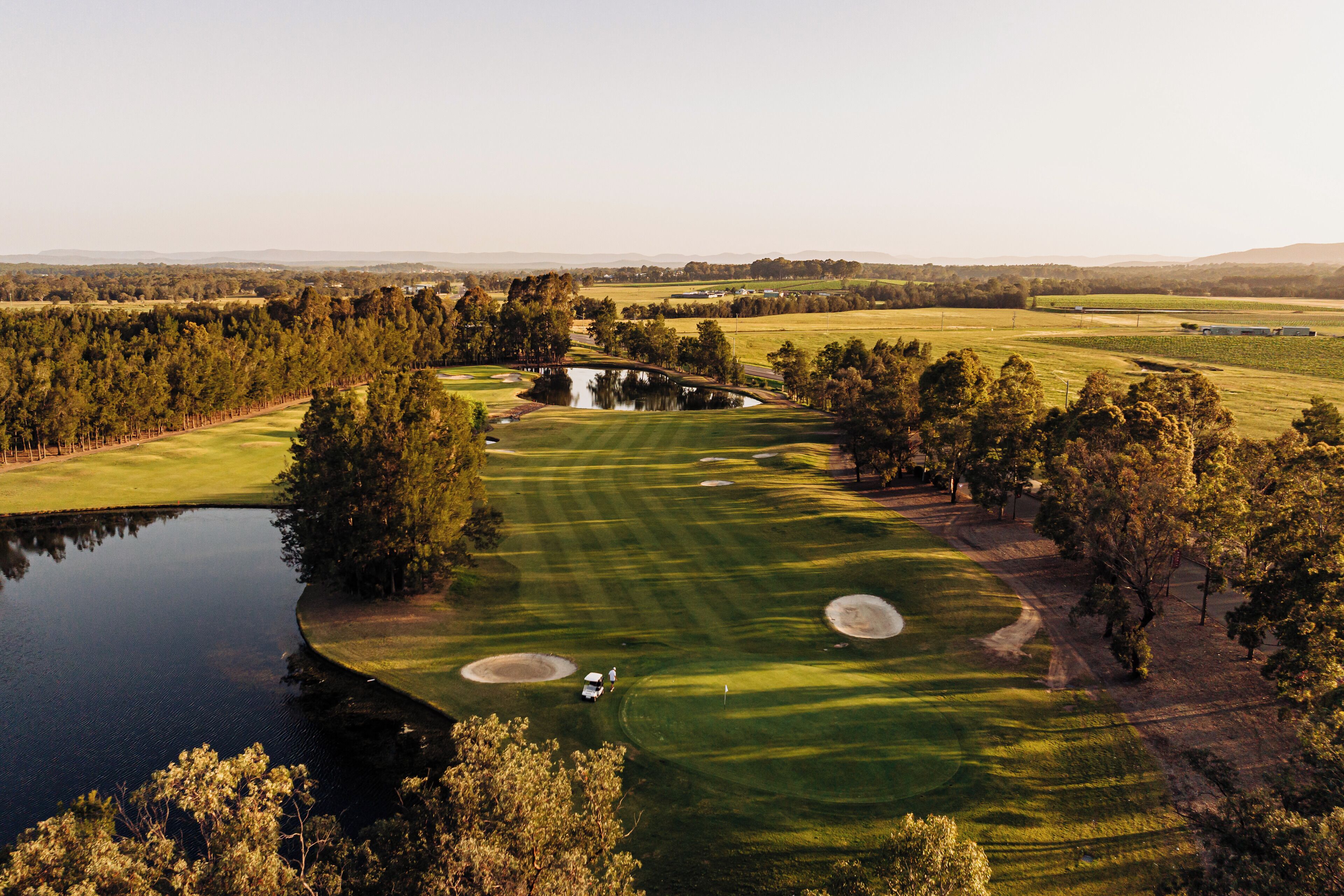 A golf course with a pond, trees, and a bridge.