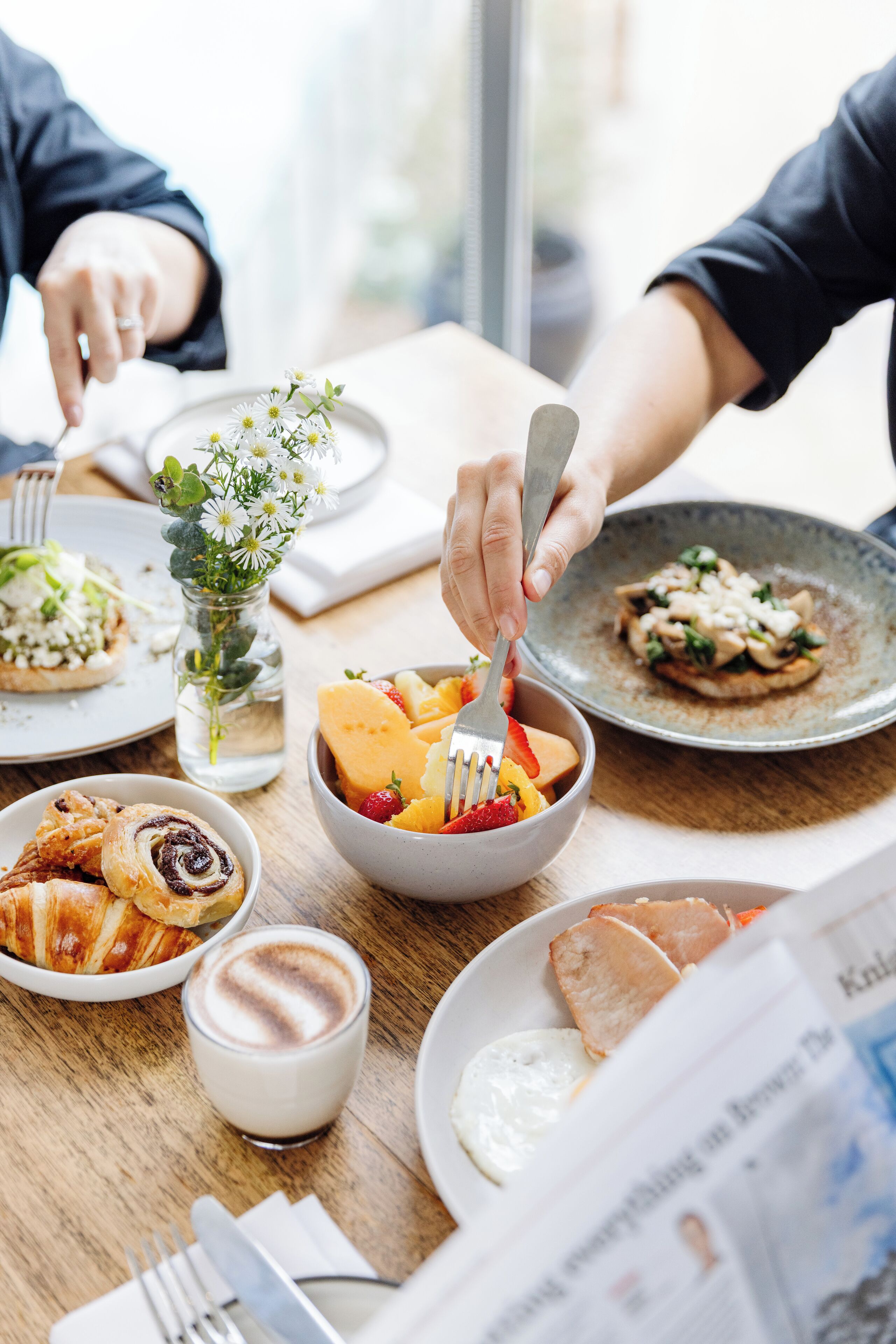 A dining table with various dishes, including a bowl of fruit, a croissant, and a glass of milk.