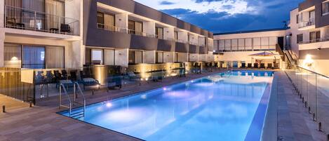 Un hotel moderno con piscina, varios balcones y un espacio exterior bien iluminado.