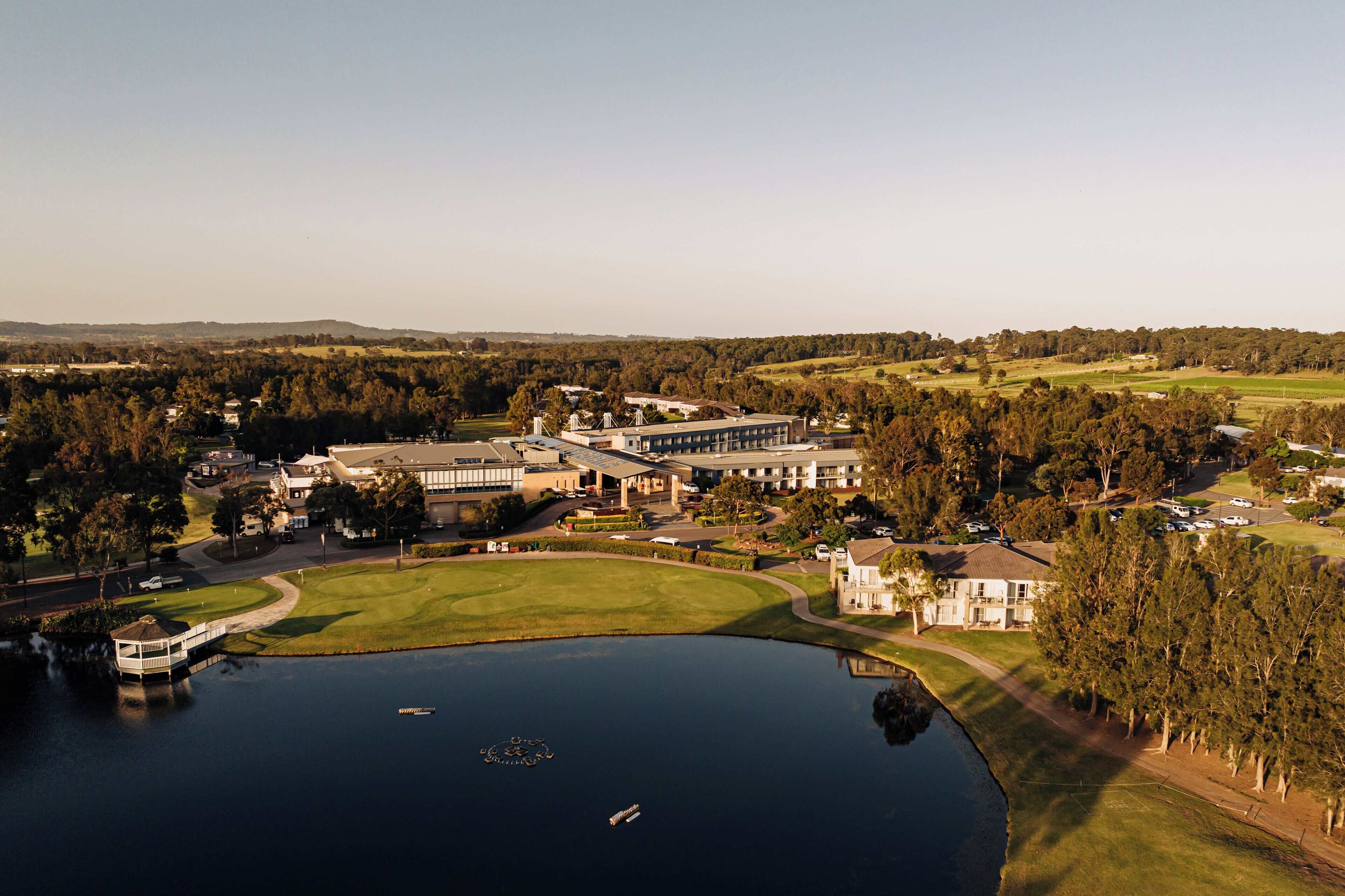 Vista aerea di un campo da golf con un club house, un edificio importante e un lago.