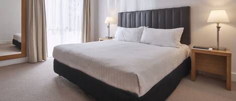 A neatly made bed with a dark headboard, two bedside tables with lamps, and a large mirror on the wall.