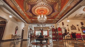 An opulent lobby with a grand chandelier, ornate ceiling, and luxurious seating.